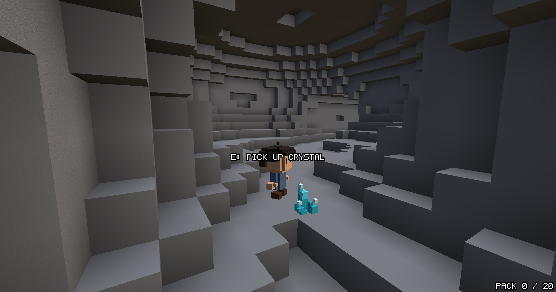 The player in a grey cave chamber beside a small blue crystal on the floor, with a prompt above reading E: pick up crystal.