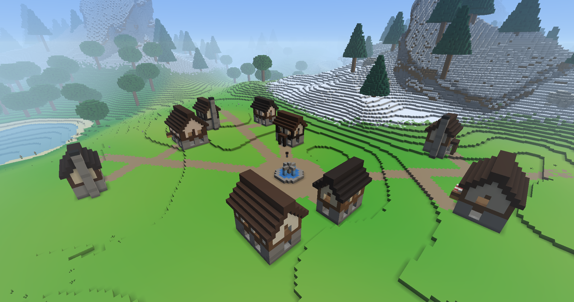 A town seen from above: timber-framed houses with brown roofs round a dirt square with a blue fountain in the middle, dirt roads running out across the grass, a lake to the left and snowy pine slopes to the right.