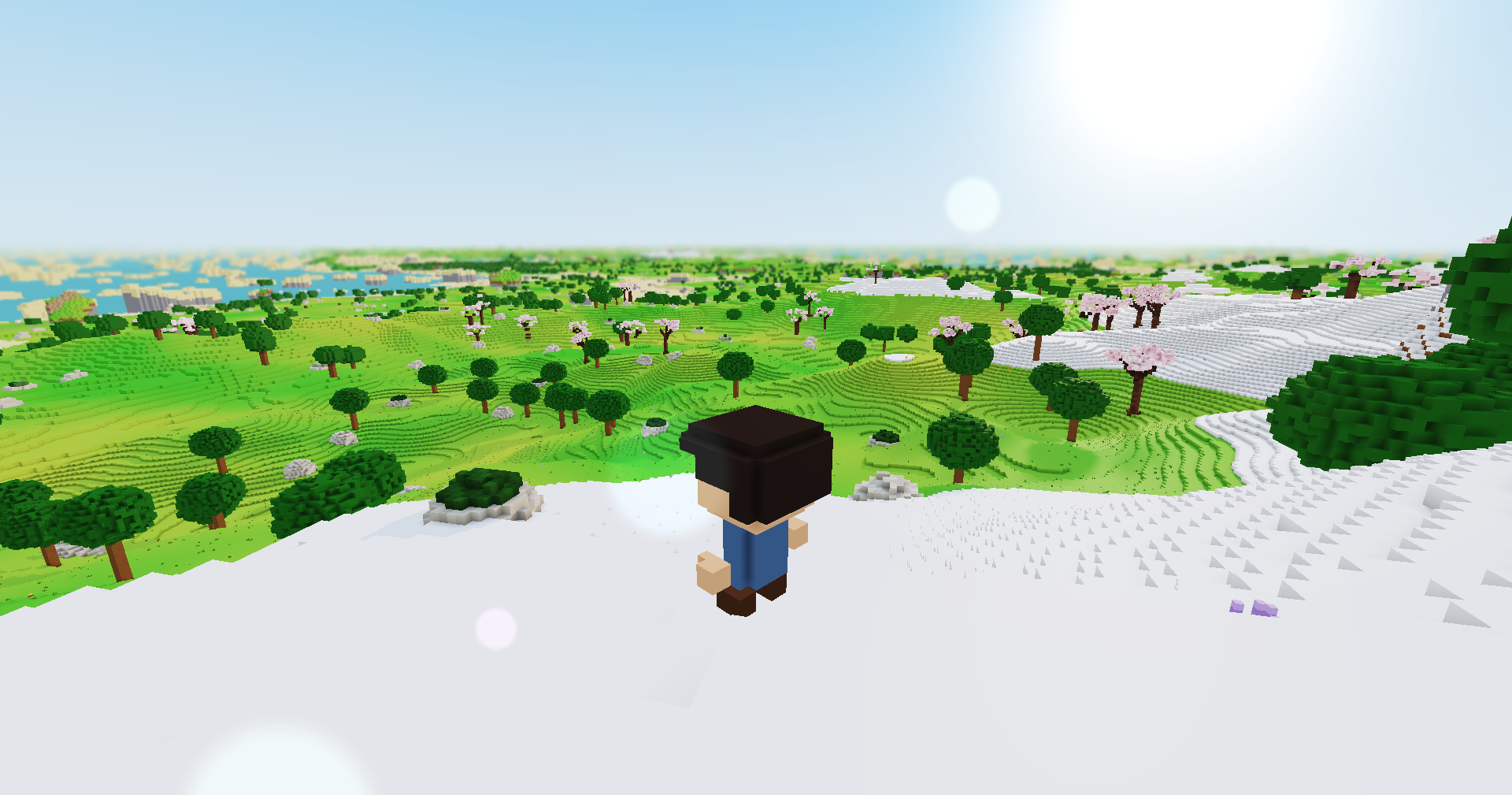 The player stands on a snowy hilltop looking out over green hills and trees, sharp up close, the land growing soft toward a hazy horizon that fades into the sky.