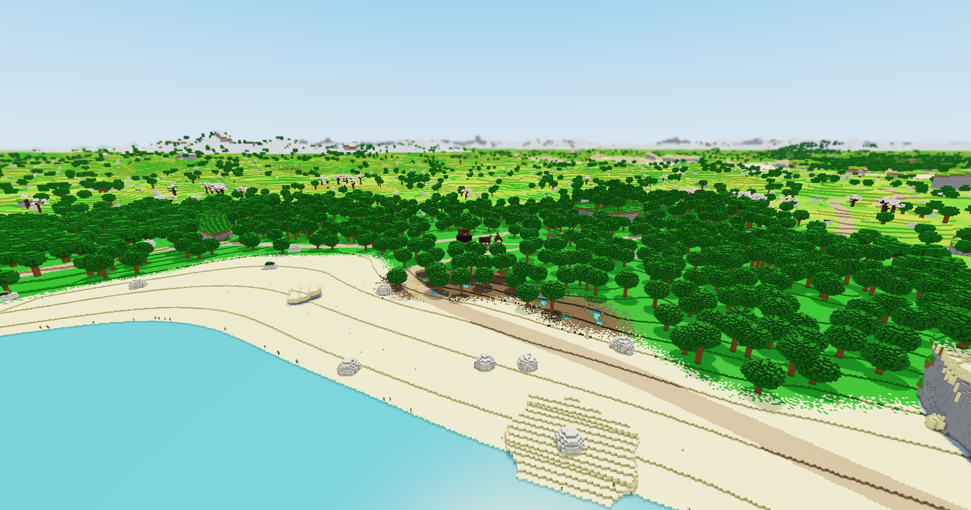 Seen from high above, a turquoise sea meets a pale sandy shore with a road along it, thick green woods behind, and the land running on to the horizon.