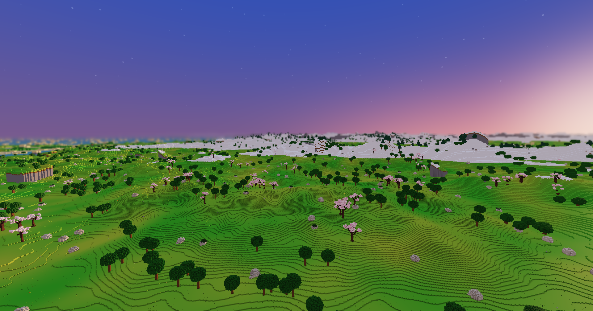 From high above at sunset, green hills and trees reaching to snowy ranges that soften into a purple and pink sky.
